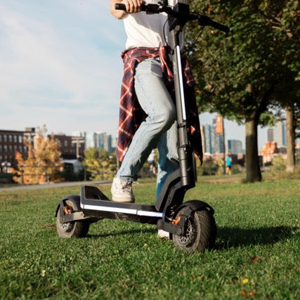 Person riding an electric scooter on a grassy path in a park.