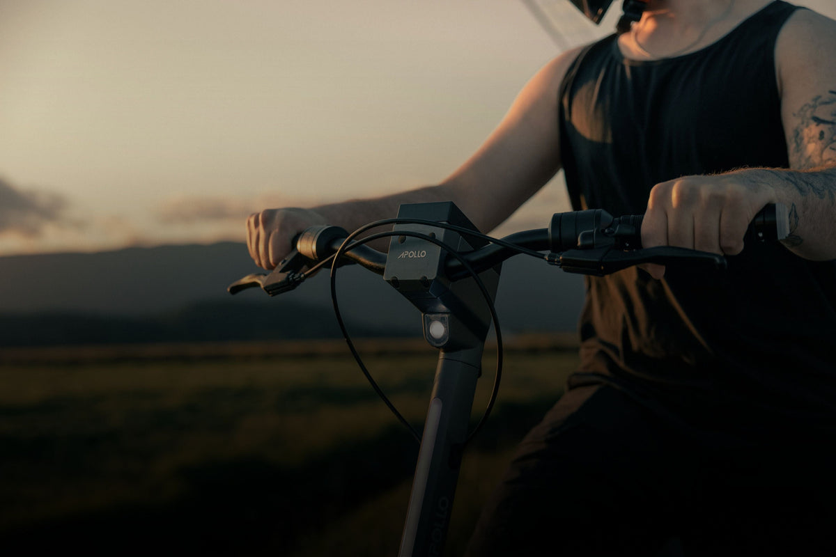Close-up of a person riding an Apollo electric scooter at sunset.